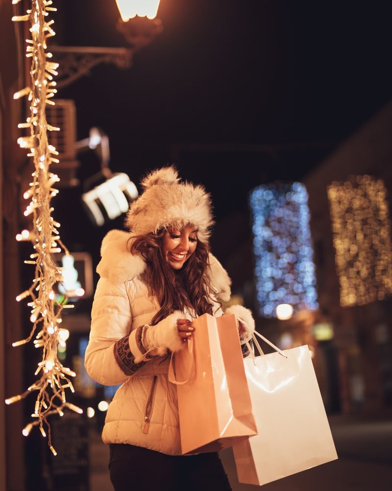 Woman holding shopping bags on a festive city street at night